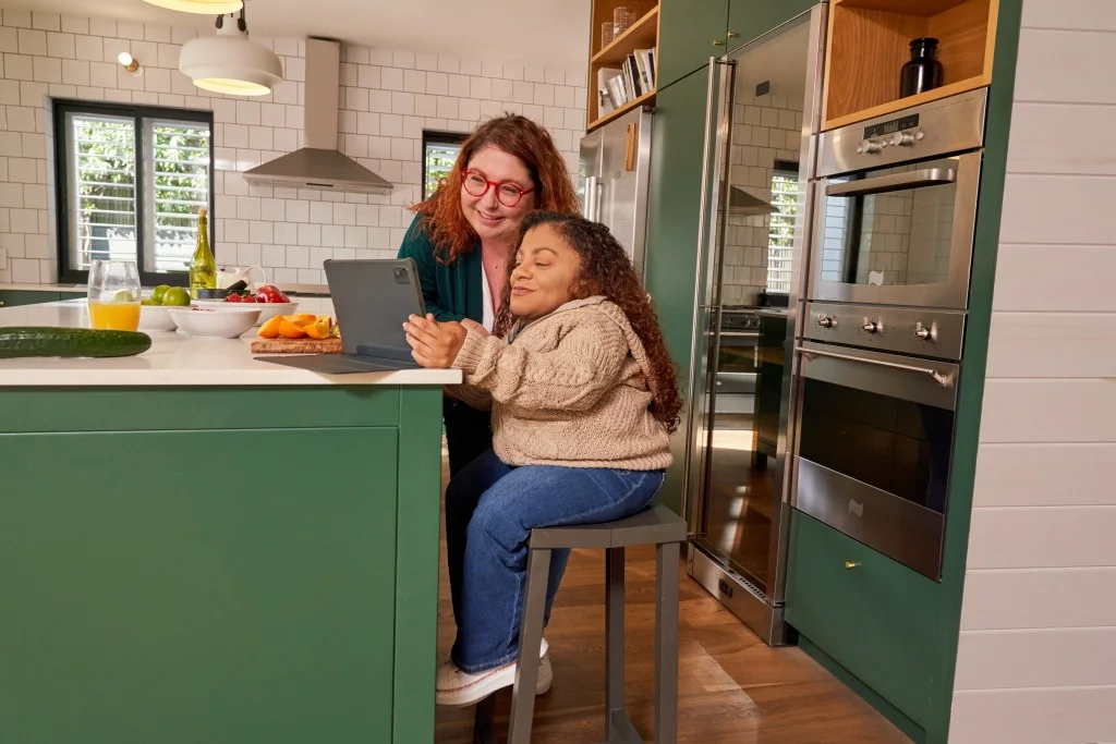 Happy disabled woman sitting at kitchen bench and smiling with support worker