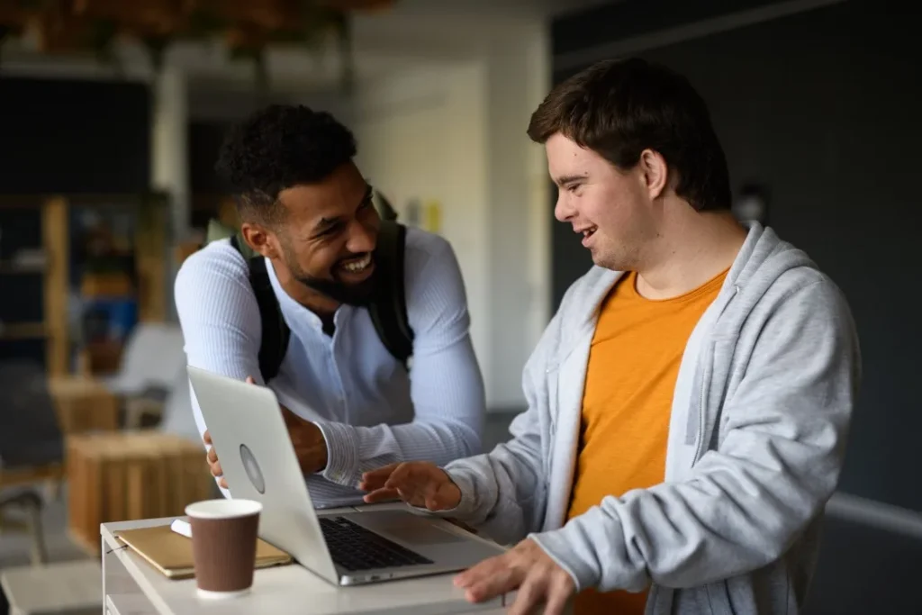 Disabled man talking with support worker while looking at laptop together